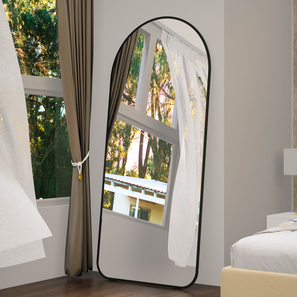 Full-length arched floor mirror with black frame leaning on the floor.