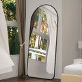 Full-length arched floor mirror with black frame leaning on the floor.