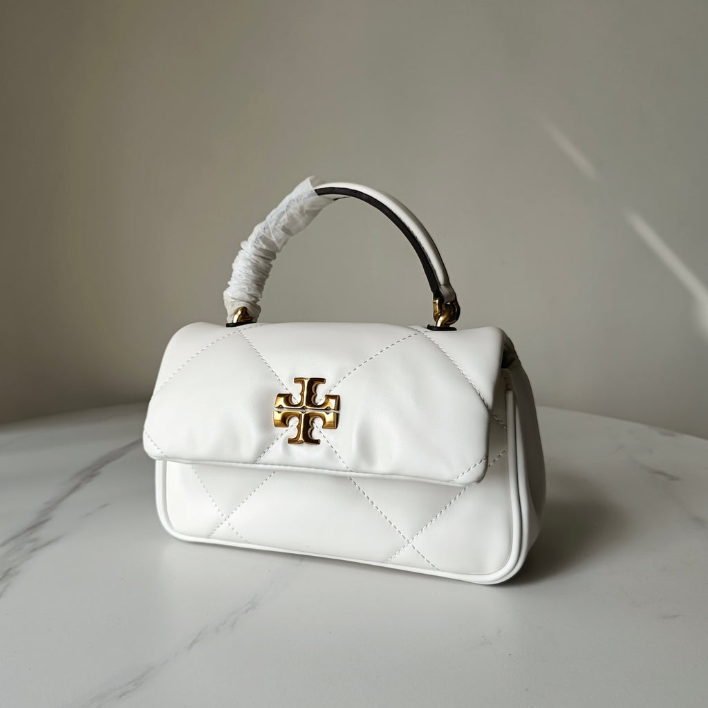 White quilted crossbody bag with gold logo clasp, rounded top handle, angled side view