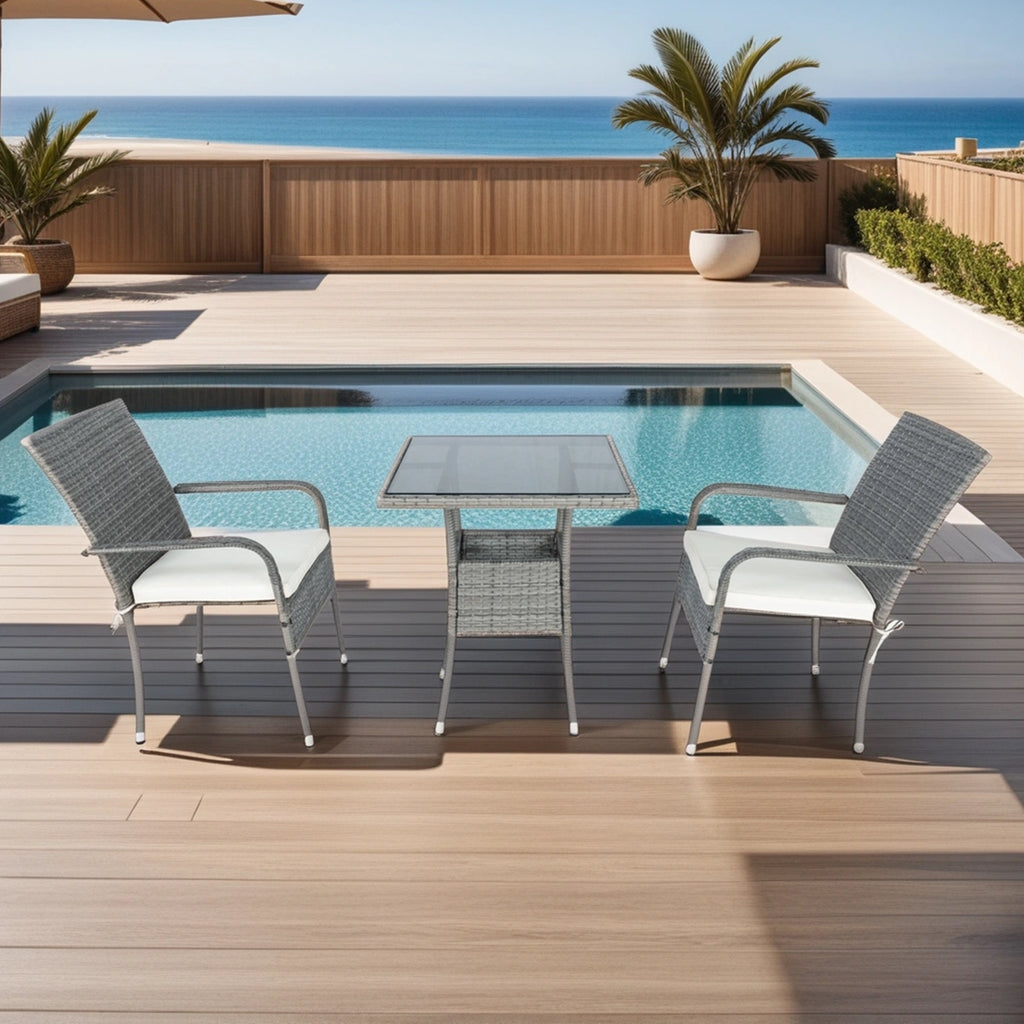 Grey wicker patio conversation set with two chairs, white cushions, and glass-top table by pool