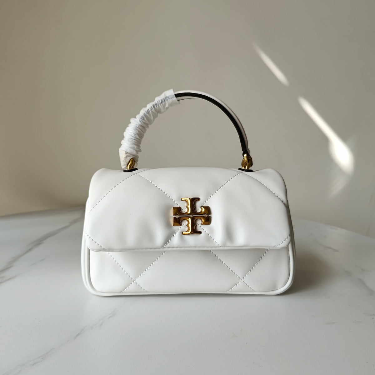 White quilted crossbody bag with gold logo clasp and curved top handle, front angle