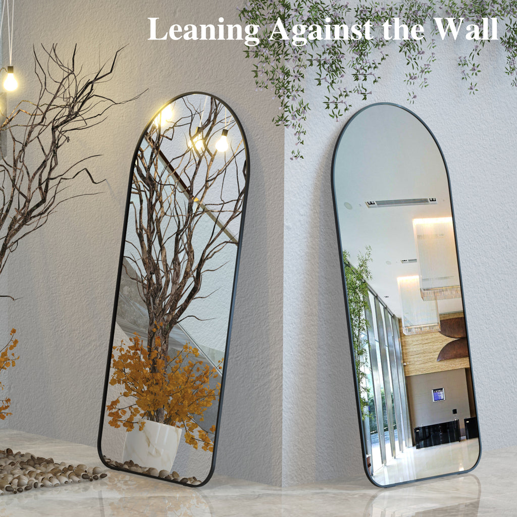 Two arched floor mirrors with black frames, leaning against a wall.