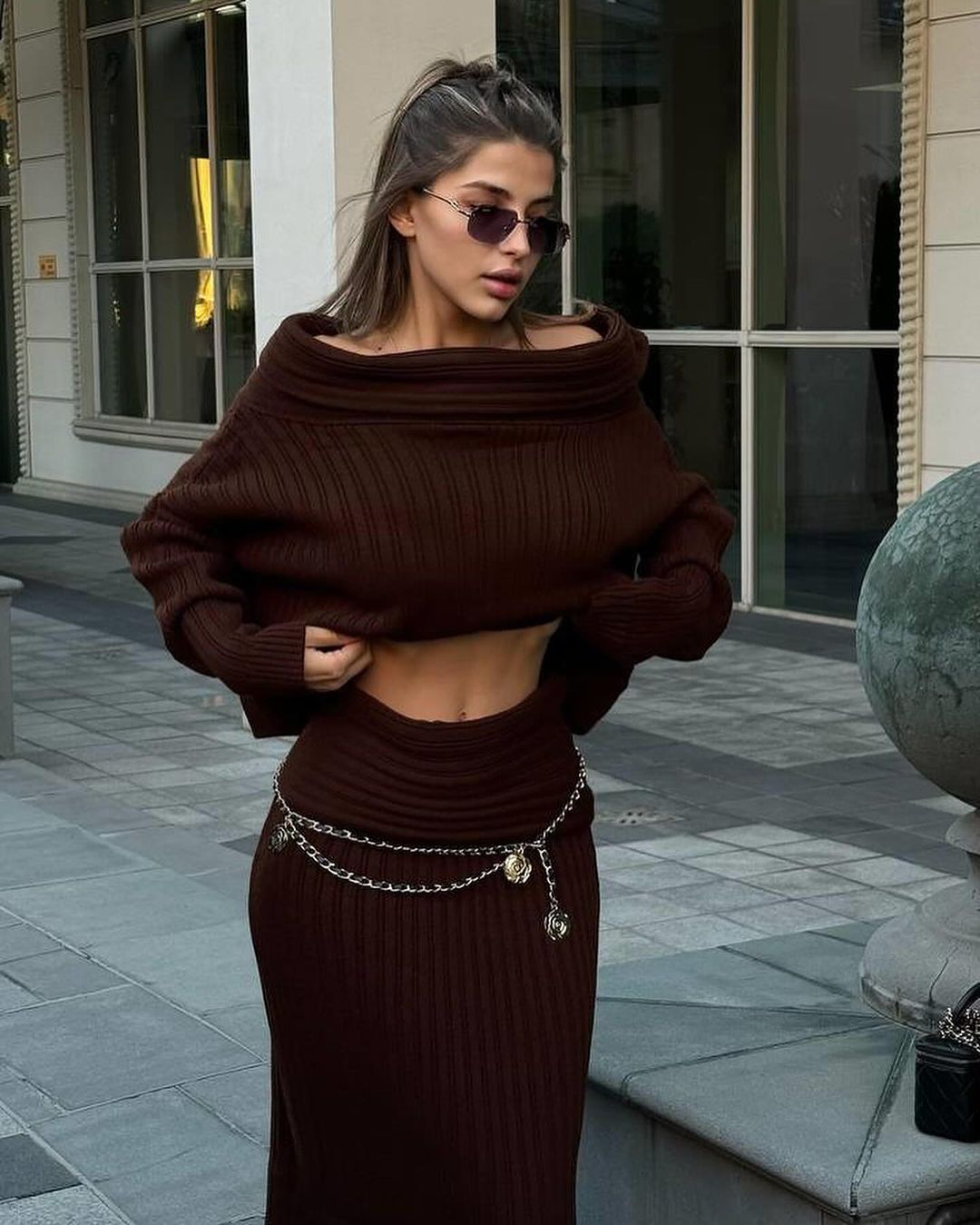 Brown off-shoulder ribbed knit sweater with matching long knit skirt set, standing