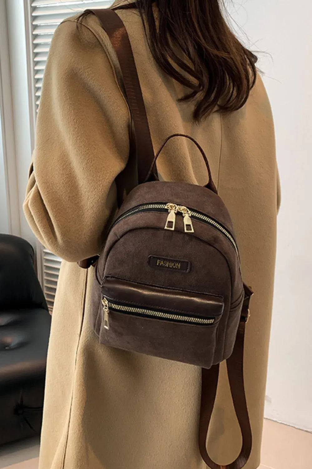 Suede brown mini backpack worn on shoulder, front zipper pocket and adjustable strap