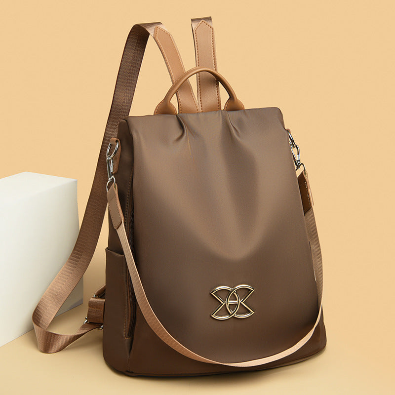 Brown backpack with curved flap, gold logo emblem, top handles and side shoulder straps