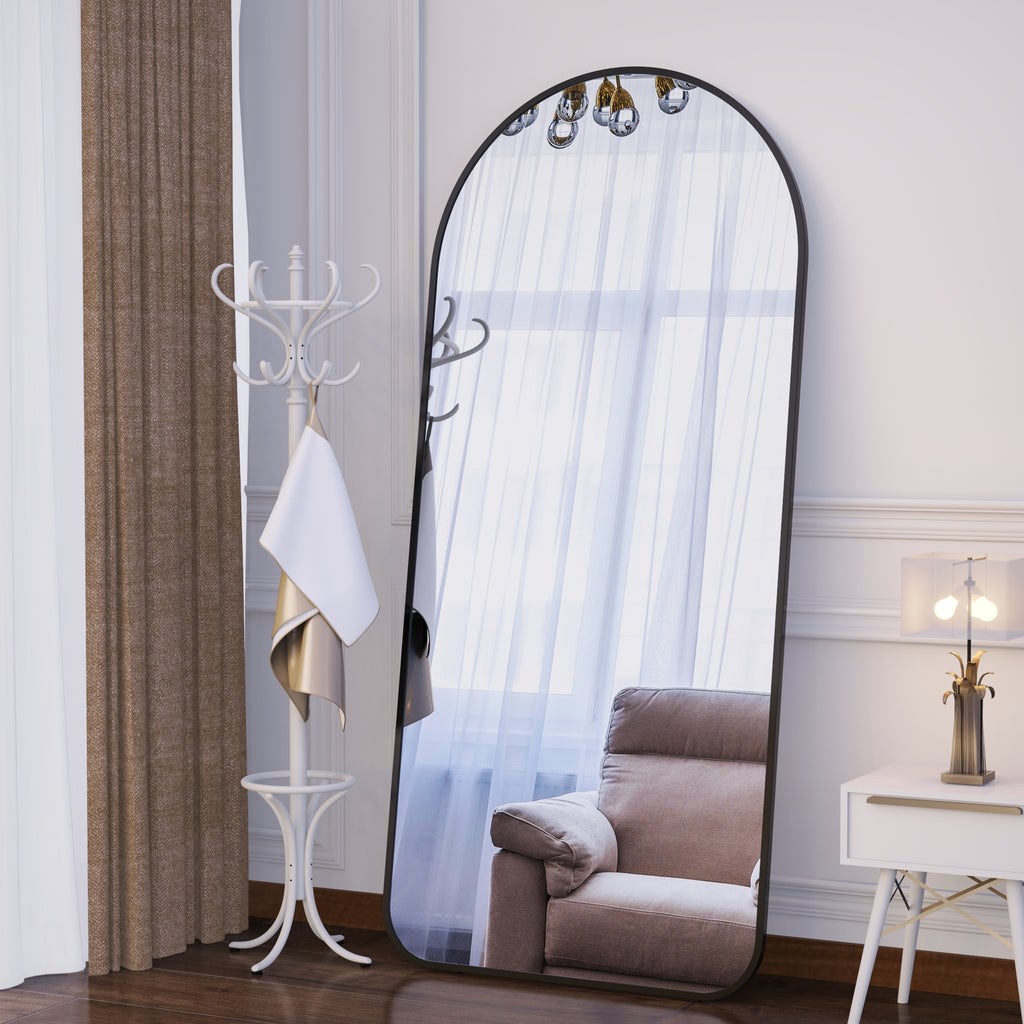 Arched full-body floor mirror with dark frame reflecting window curtains