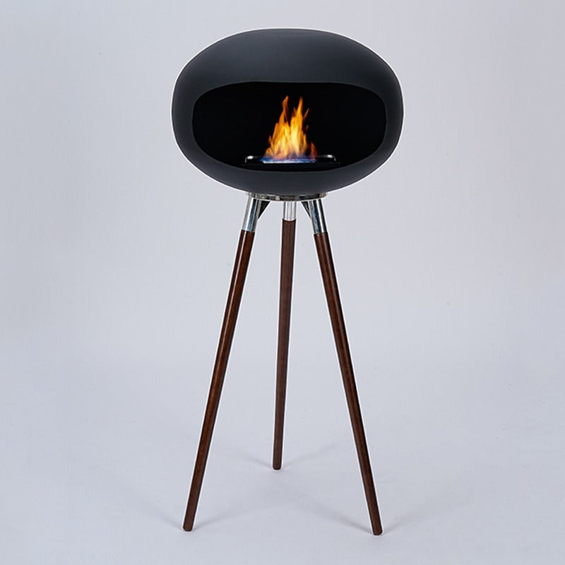 Black round ethanol fireplace bowl on three wood tripod legs, with visible flame inside.