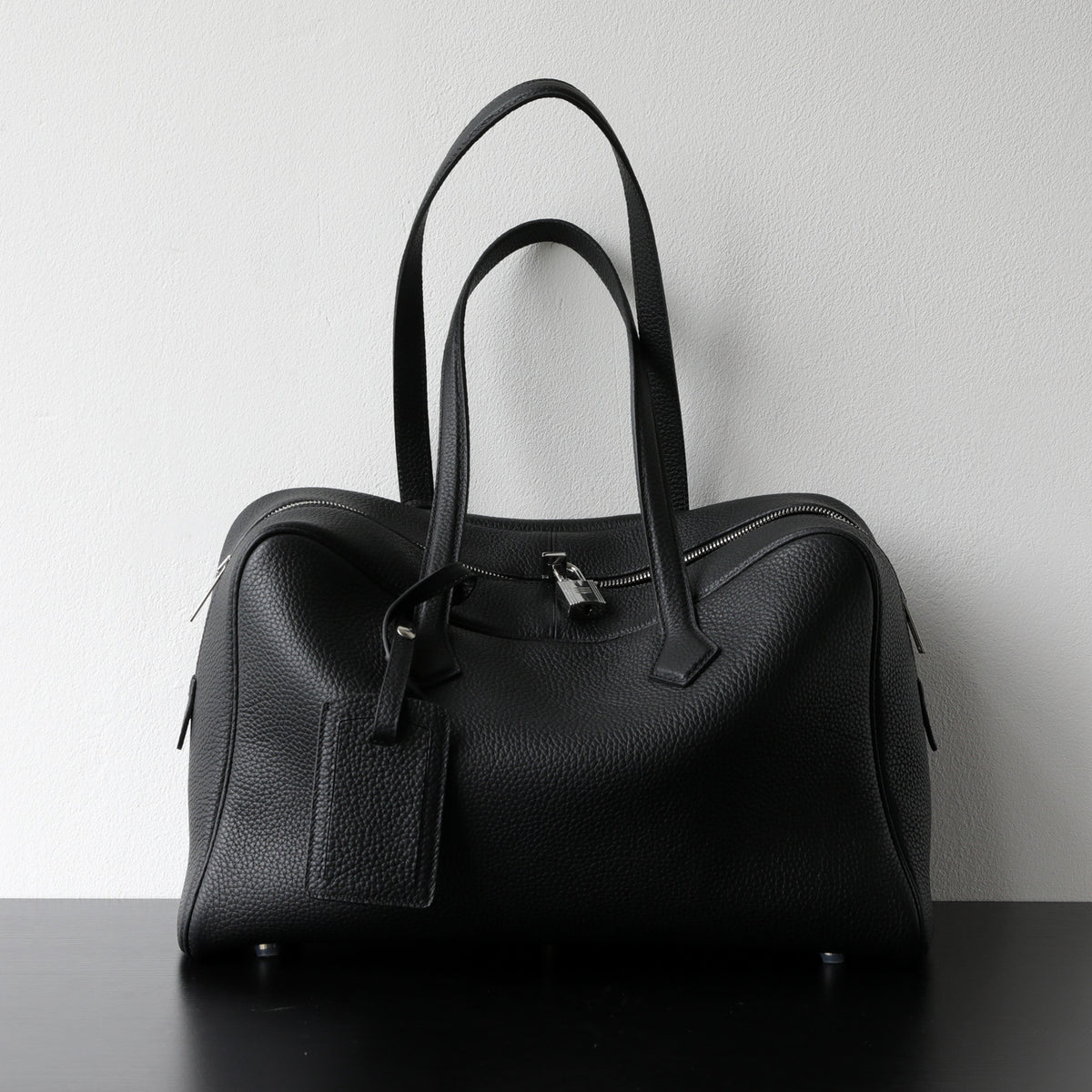 Black leather-look crossbody bag with top handles, front zipper, and detachable strap