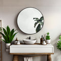 Round bathroom mirror with black metal frame and reflective glass, plant reflections visible