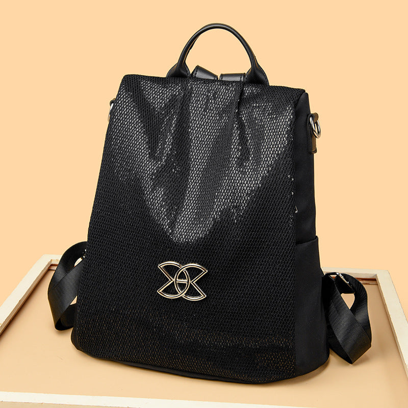 Black textured backpack with gold logo emblem, top handle and side shoulder straps