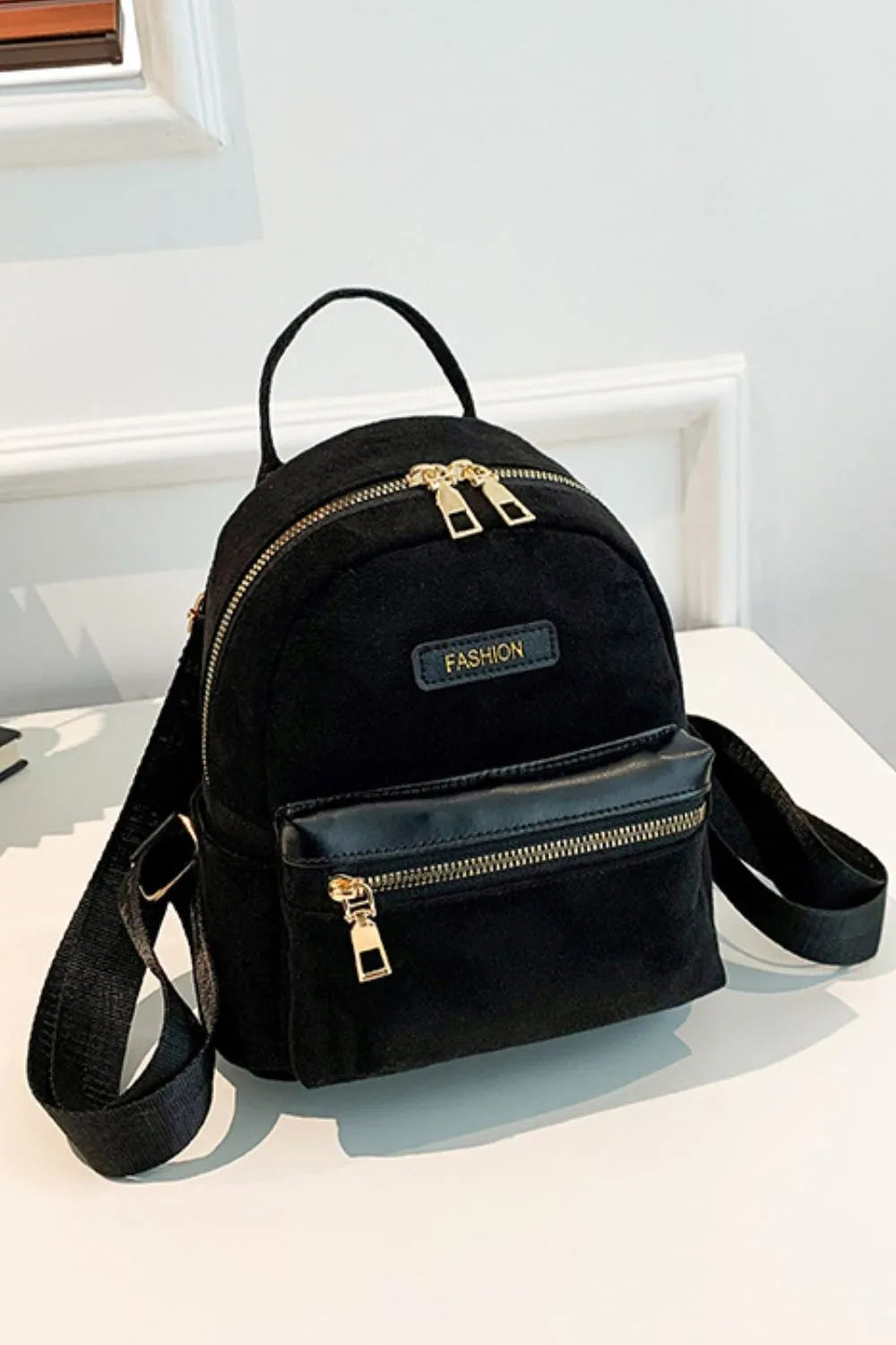 Suede black mini backpack on table with front zipper pocket and adjustable strap