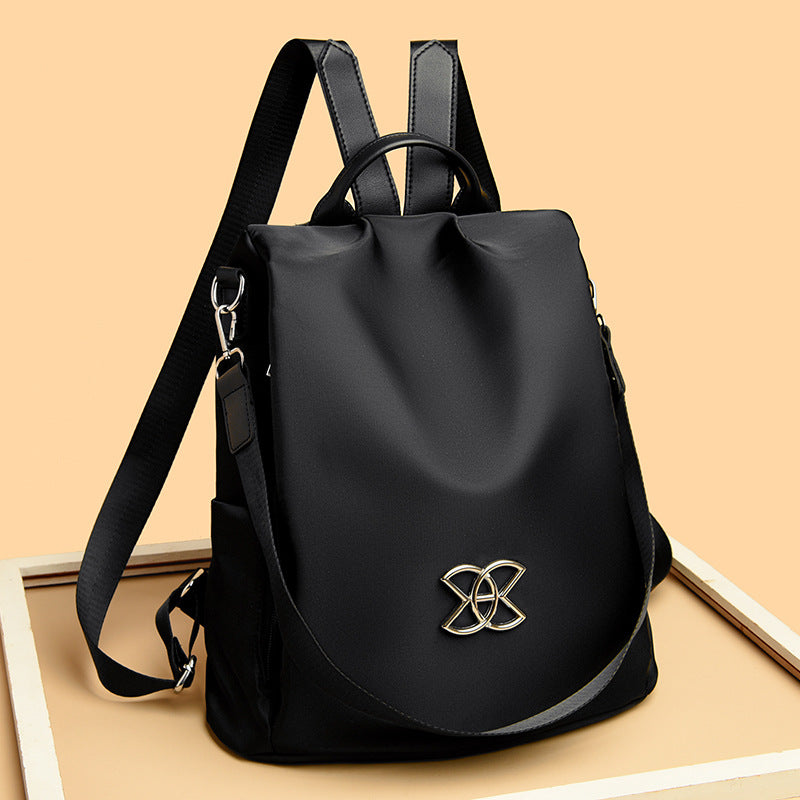 Black backpack with front flap and gold logo emblem, adjustable shoulder straps