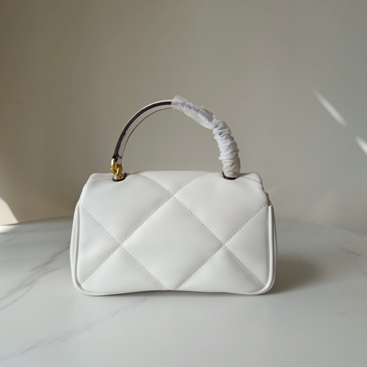 White quilted handbag with gold clasp, short top handle, diagonal diamond stitching