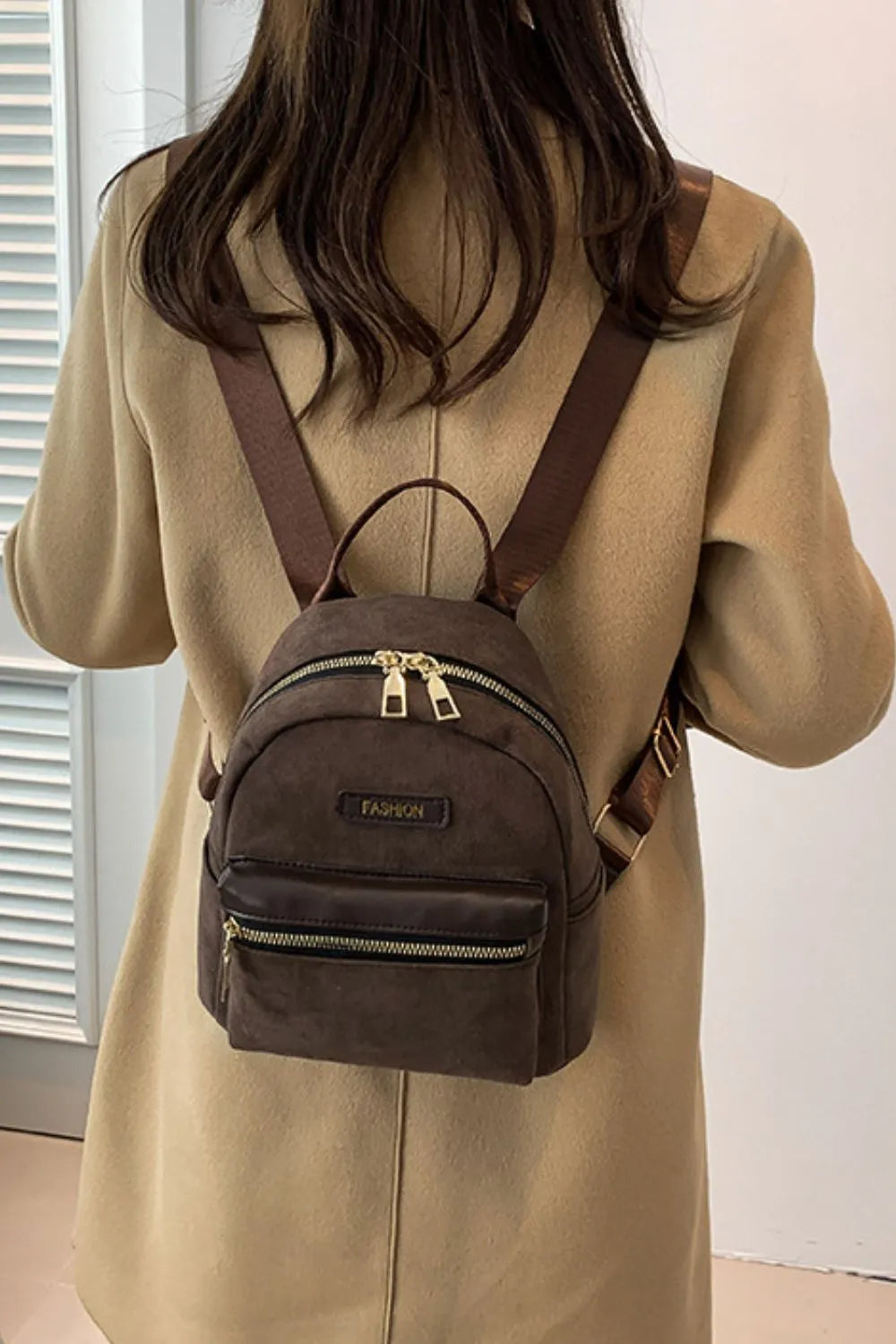 Suede brown mini backpack on model, top handle and front zipper pocket with strap
