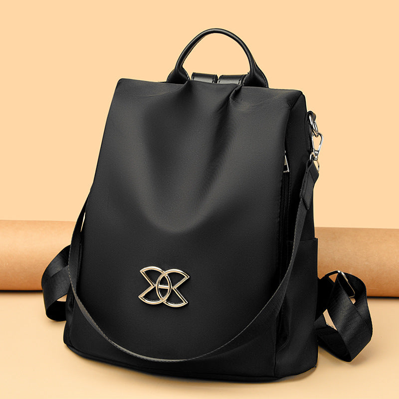 Black backpack with curved flap and gold logo emblem, top handle and shoulder straps