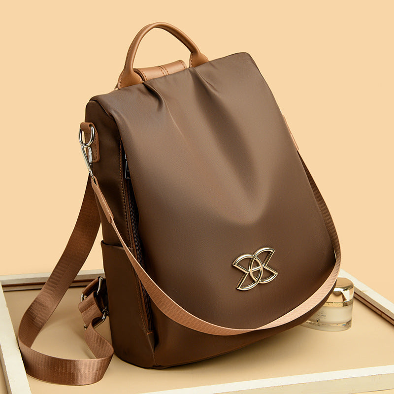 Brown backpack with curved flap, gold logo emblem, top handle and shoulder straps