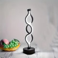 Black bar table lamp with looped silhouette frame and round base, lit white glow