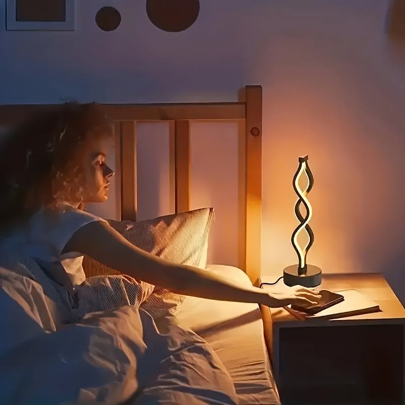 Black loop bar table lamp with round base, glowing warm white beside bed