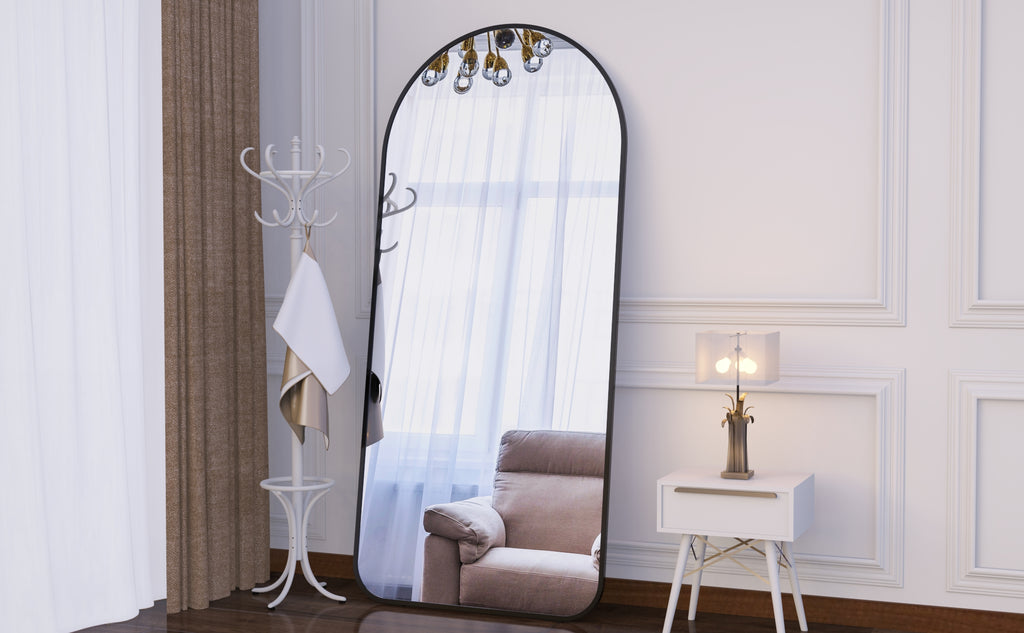 Full-length arched floor mirror in dark frame beside coat stand and table